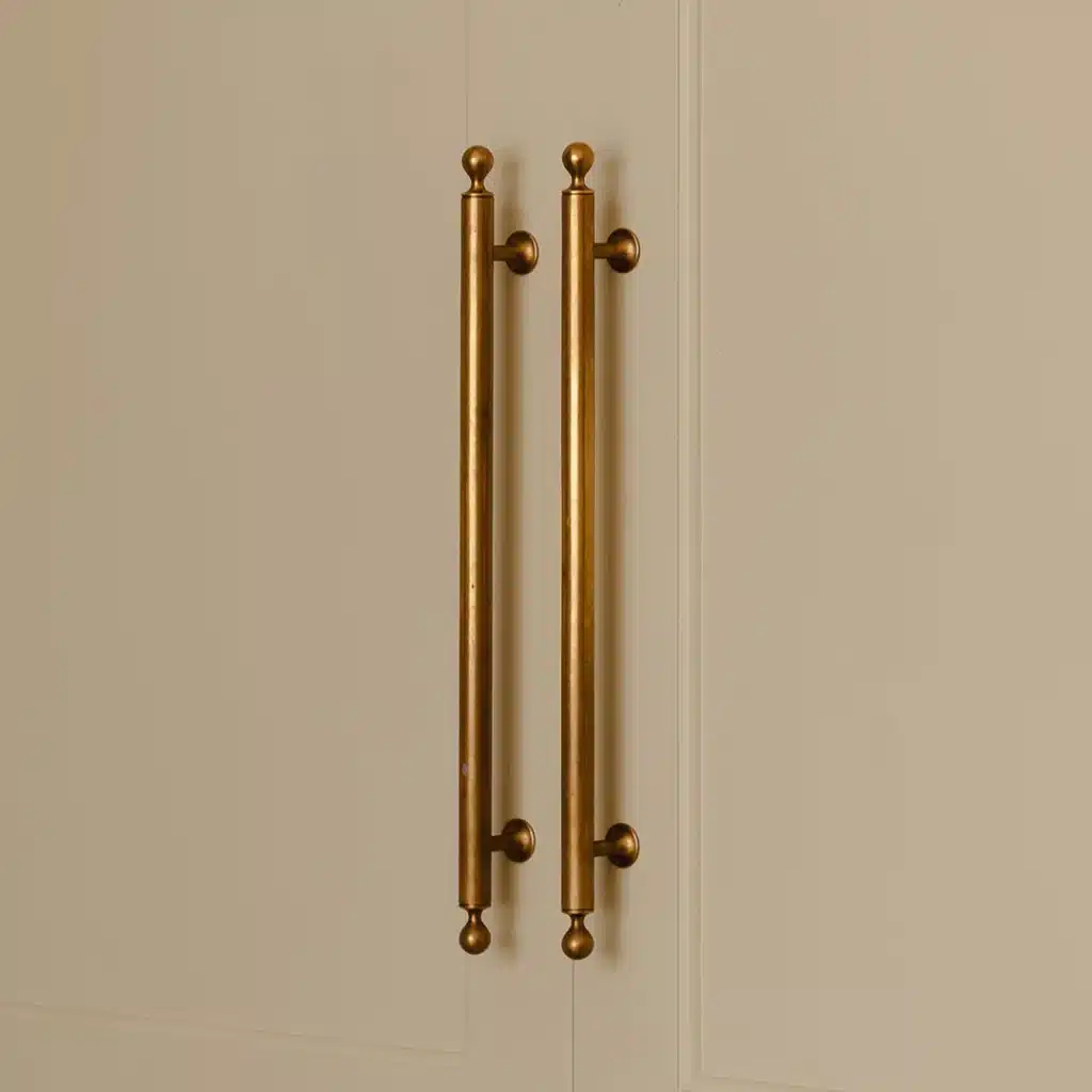 Two brass cabinet handles vertically mounted on a cream-colored cabinet door fall along the center.