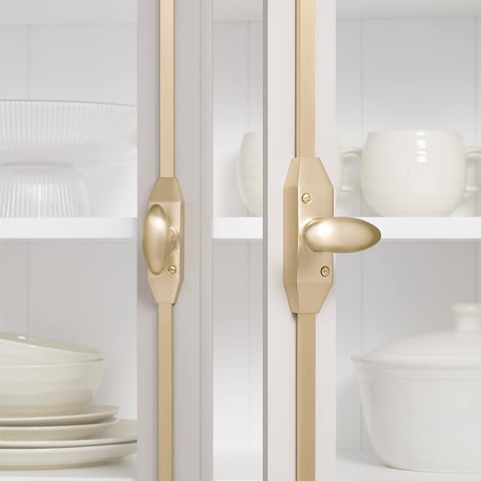 Glass-front kitchen cabinet with gold hardware, showing white plates and bowls inside behind the doors.